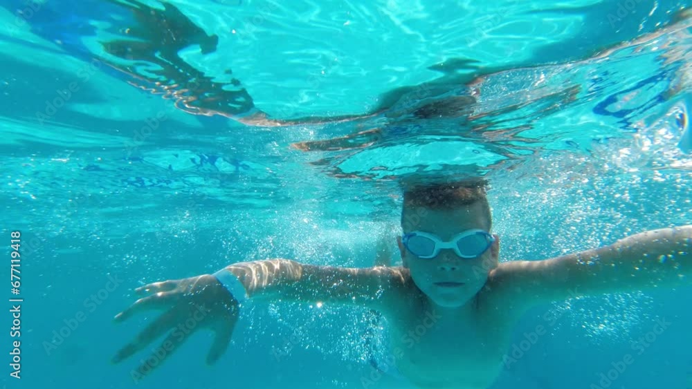 A boy swims underwater in a pool wearing safety goggles and enjoys his vacation A boy swims underwater in a pool wearing safety goggles and enjoys his vacation