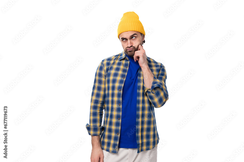 young pensive smart European brunette man with a beard and mustache is dressed in a yellow hat and blue shirt on a white background with copy space