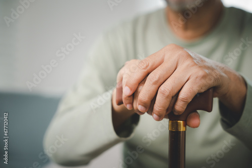 Close up hands of Asian Elderly hand holding handle of cane, senior disabled man holding walking stick, Old man sitting resting at home hold wooden walking cane, International Day for the Elderly photo