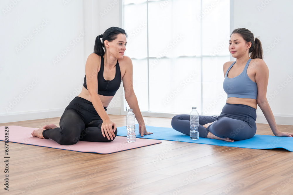 female yoga instructor sits and chats on a yoga mat with a friend to practice yoga together. They are happy to work together to complete the exercise and take a drink break in the gym female yoga instructor sits and chats on a yoga mat with a friend to practice yoga together. They are happy to work together to complete the exercise and take a drink break in the gym