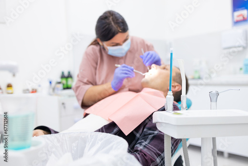 Side view of female dentist examining male patient with tools in dental clinic