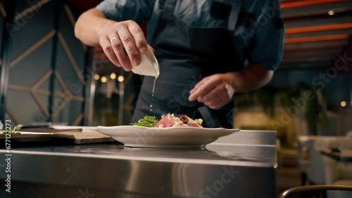 A chef holds a cup of oil and dresses a bruschetta with it in the kitchen of an Italian restaurant