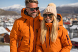 Happy middle-aged couple dressed in a yellow sports jacket, wearing glasses in sunny winter weather against the backdrop of the village and mountains