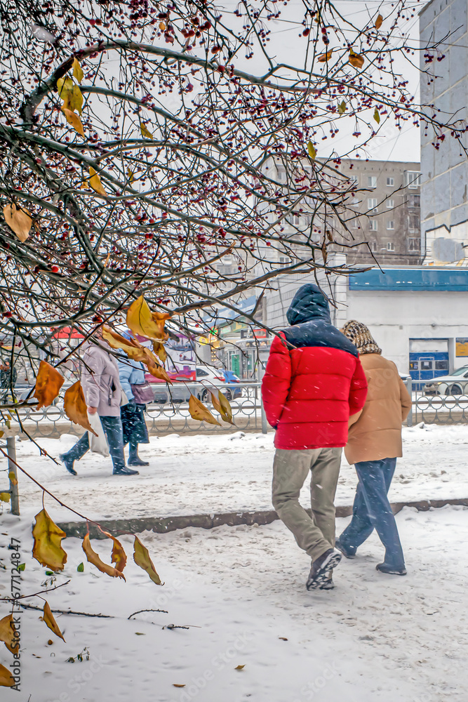 People walk along the snow-covered sidewalk on an autumn day People walk along the snow-covered sidewalk on an autumn day