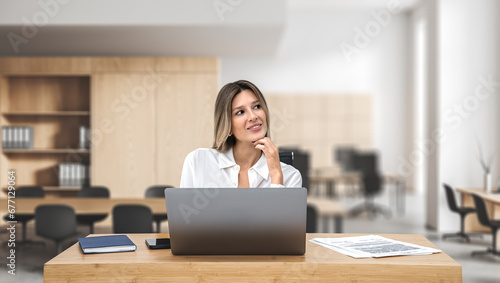Pensive woman with laptop sitting at office desk