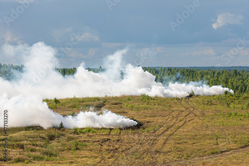Heavy combat vehicles tanks drive around the butts and put up a smoke screen