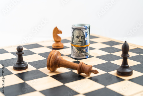 Chess game, white king defeated, black pawn and bishop standing, rolled 100 dollar bills as chess piece. Concept dollar leadership and competition.