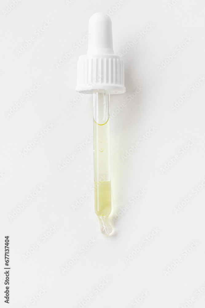 Pipette with golden serum or gel or serum, yellow on a light background.