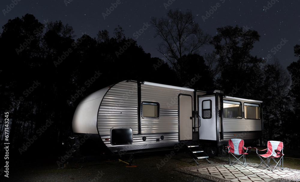 Stars in the sky above an RV with a forest silhouetted behind. Stars in the sky above an RV with a forest silhouetted behind.
