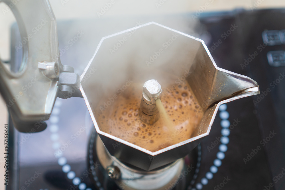 Chimney of stove-top moka pot is flinging out crema espresso coffee and also has smoke steam or smog. Moka pot is placed on induction cooktop. Chimney of stove-top moka pot is flinging out crema espresso coffee and also has smoke steam or smog. Moka pot is placed on induction cooktop.