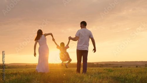 Parents, daughter run at sunset, kid holds hands of his parents and jumps. Active family playing in meadow with their daughter at sunset, teamwork. Happy family warm autumn day in park. Family, nature © zoteva87
