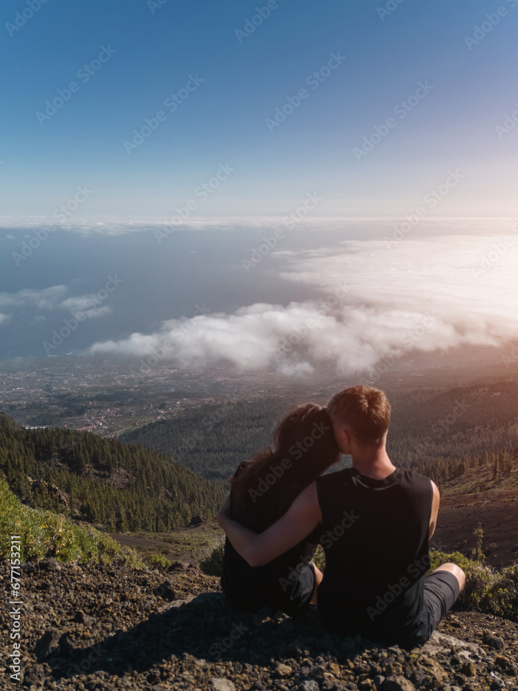 romantic lovely couple sitting on mountain top above clouds and looking on view