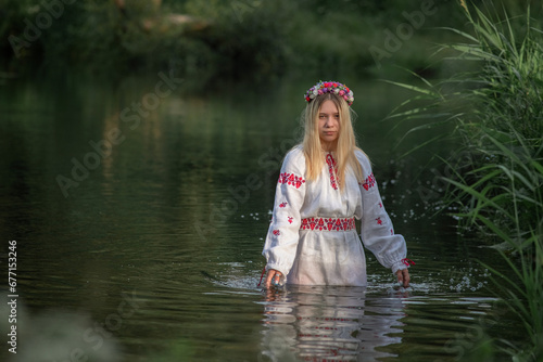 Fototapeta Naklejka Na Ścianę i Meble -  A young beautiful blonde girl in a national costume in the river.
