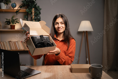 Female influencer recording video blog about unboxing of new VR Glasses, doing review of modern gadget at home. photo