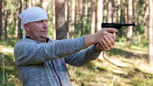 A man in the woods on a sunny summer day having fun and learning to shoot at a target with his German air pistol. photo