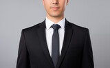 Man in a black suit, white shirt and black tie isolated on a gray background. Young top manager in a business suit