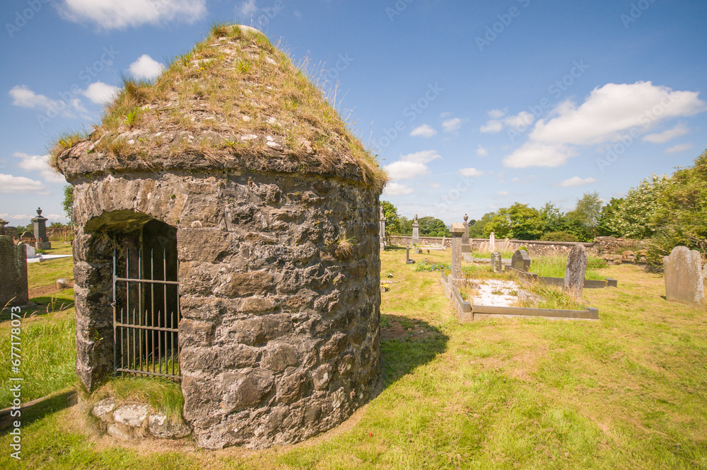 Round stone burial chamber with stone roof in a graveyard
