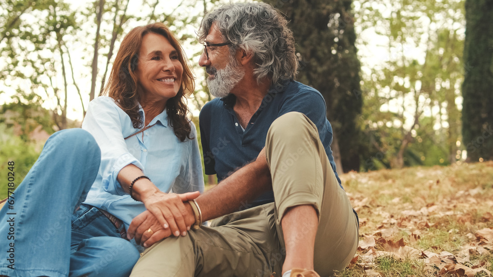 Beautiful retired couple spending time together outside, sitting on the grass in the park in autumn Beautiful retired couple spending time together outside, sitting on the grass in the park in autumn