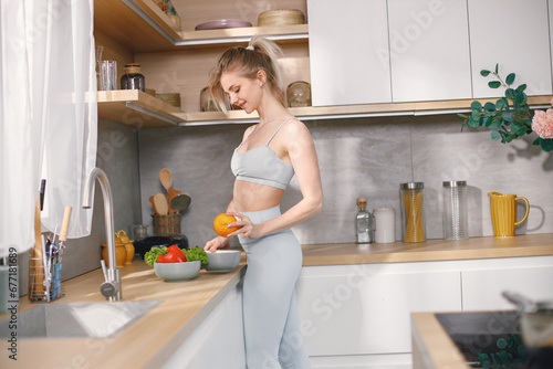 Fit woman in grey sportive costume standing on a kitchen with fresh fruit