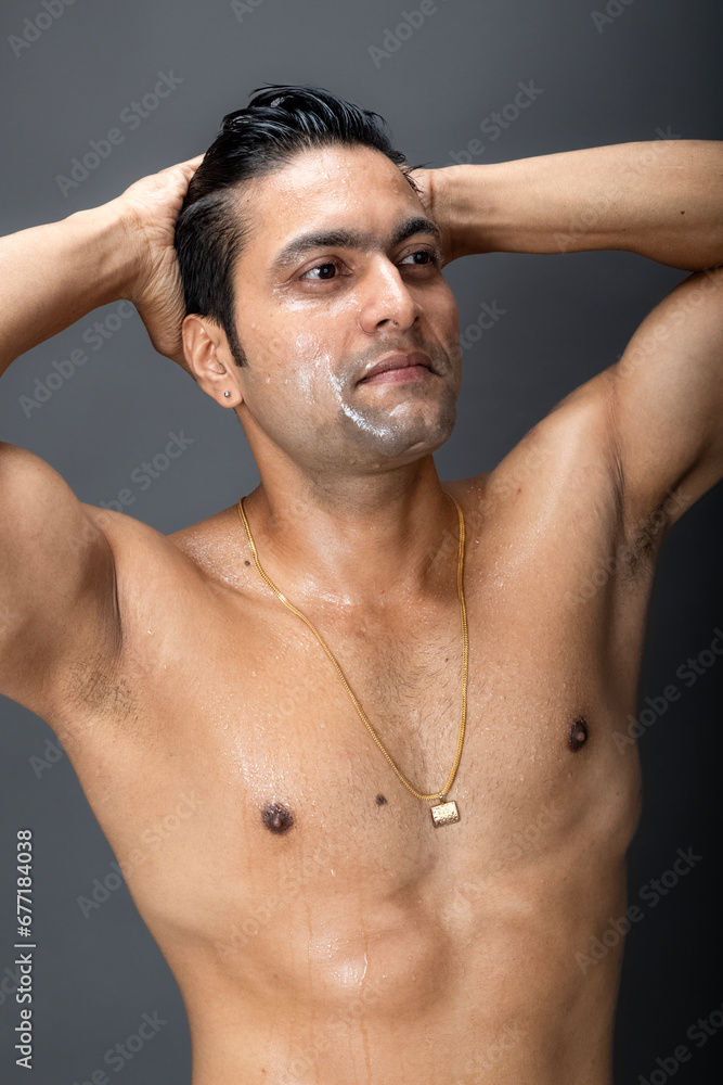 Portrait of a shirtless young man. Healthy muscular man with black hair, posing with hands behind head on grey background. Portrait of a shirtless young man. Healthy muscular man with black hair, posing with hands behind head on grey background.