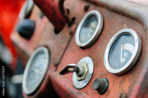 Rusty instrument panel of a red vintage farm tractor showing dials, ignition key and starter button photo