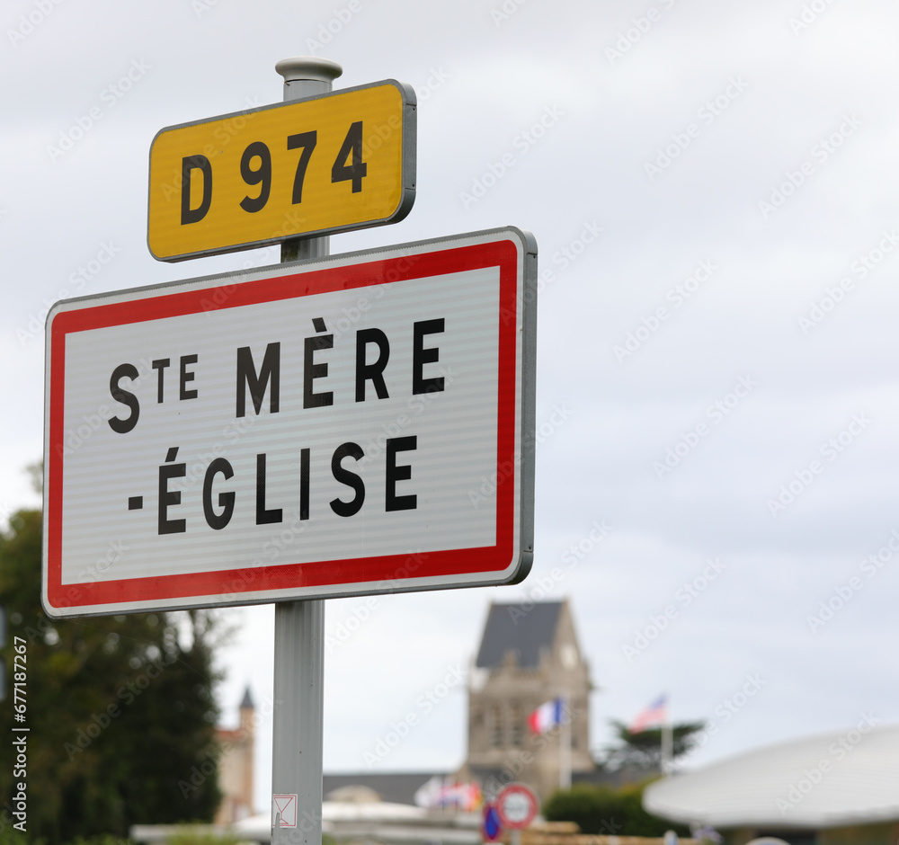 Obraz premium road sign with name of place and the church with bell tower which became symbol of the Normandy landings in France