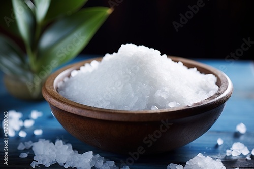 A close-up of salt crystals in a clay bowl on a blue background, with a green plant nearby.