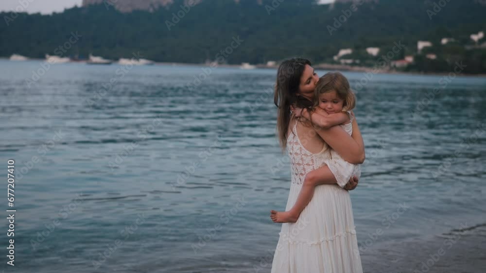 Mother holding her daughter while walking by the sea Mother holding her daughter while walking by the sea