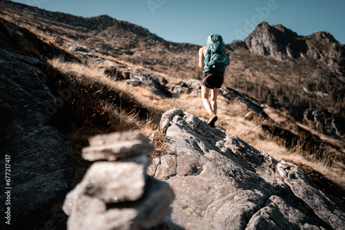 Frau-Bergsteiger mit grünem Rucksack steigt in den Alpenpfad hinauf in braunen Farben der Umgebung