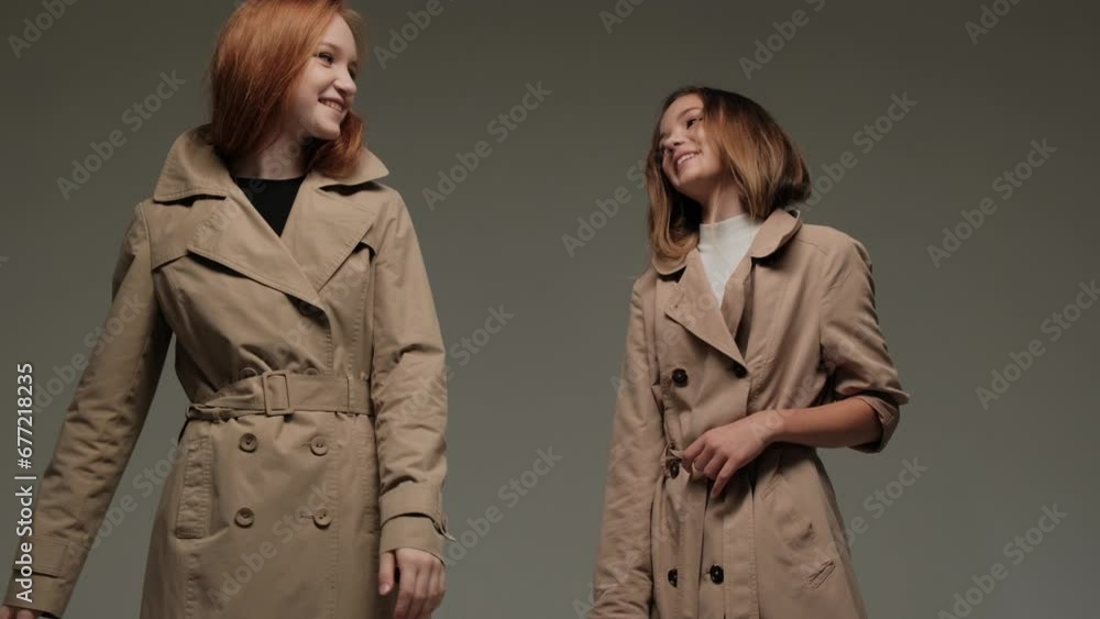 Two stylish models in a trench coat in the studio on a gray background. Two stylish models in a trench coat in the studio on a gray background.