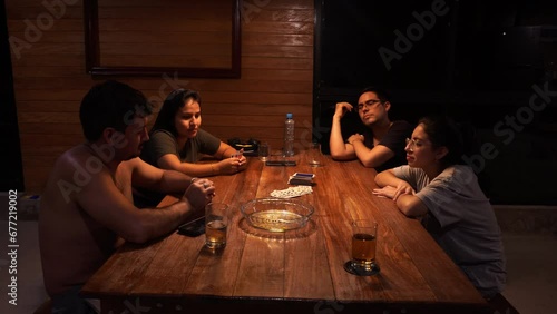 Group of young friends drinking, talking, and playing cards on a cabin table photo