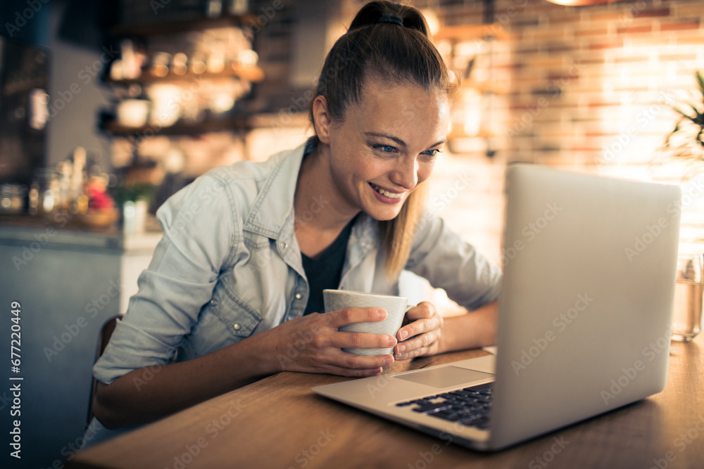 Smiling young woman with coffee cup sitting at desk with laptop Smiling young woman with coffee cup sitting at desk with laptop