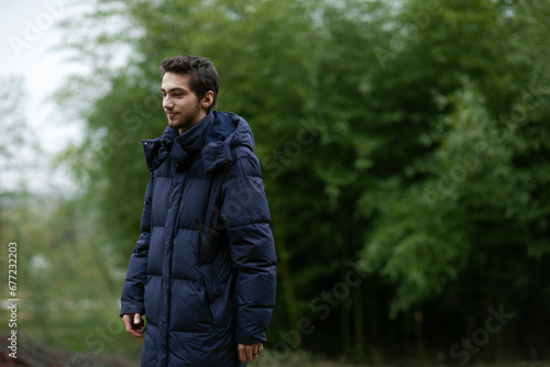Portrait of a handsome young man in park, wear in warm clothes, tree background. Copy space.