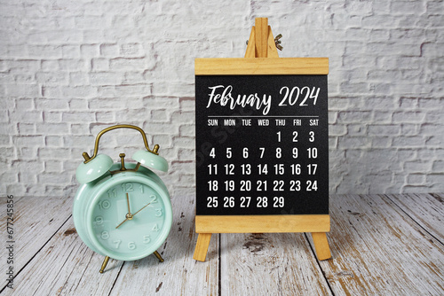 February 2024 monthly calendar and alarm clock on wooden background