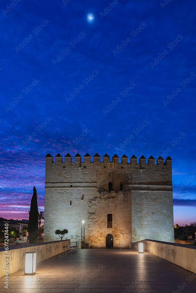 Fototapeta premium Torre de la Calahorra at the southern end of the Roman bridge of Cordoba at dawn and under a crescent, currently the living museum of Al-andalus, Andalucia.