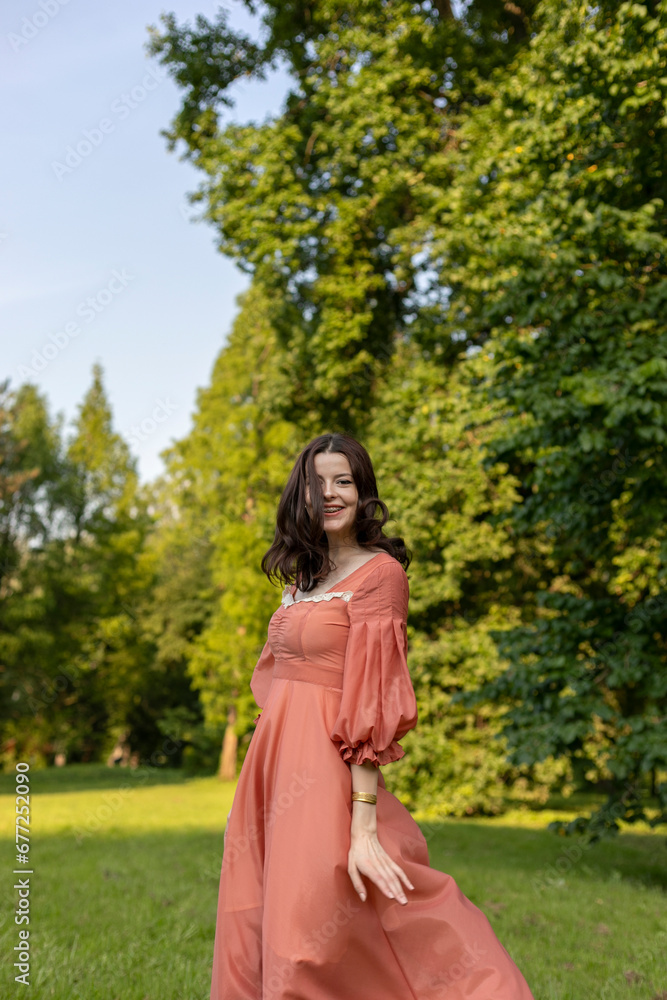 Portrait of a beautiful happy brunette girl in dress posing in the park, tree background.
