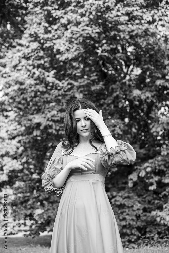 Portrait of a beautiful brunette girl in dress posing in the park, tree background. Black and white photo.
Portrait of a beautiful brunette girl in dress posing in the park, tree background. Black and white photo.