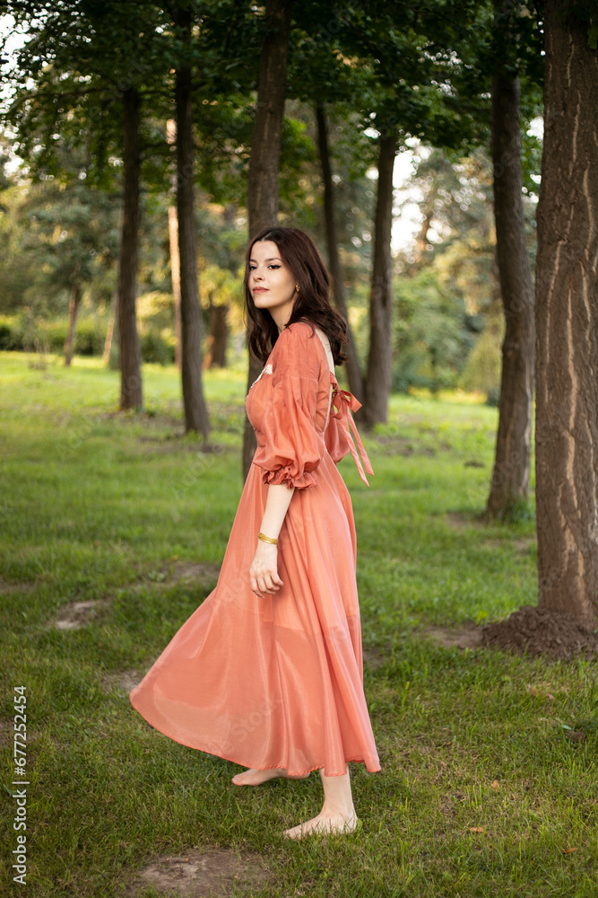 Brunette girl in beautiful dress posing in the park, tree background.
Brunette girl in beautiful dress posing in the park, tree background.