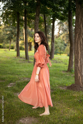 Brunette girl in beautiful dress posing in the park  tree background. 