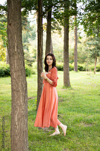 Beautiful brunette girl with makeup in dress posing in the park, tree background. 