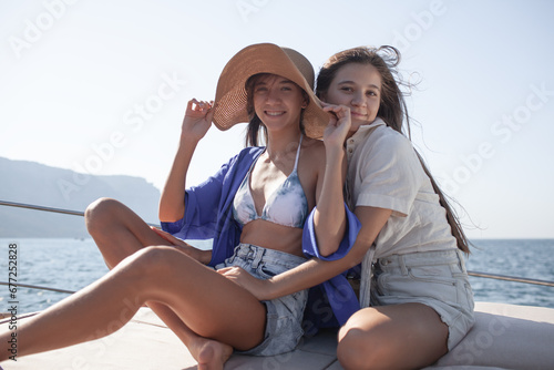 Two beautiful two girls with a slender figure travels  on a boat during a summer vacation in the open sea or ocean against the background of the island.  Friends tiurists together
