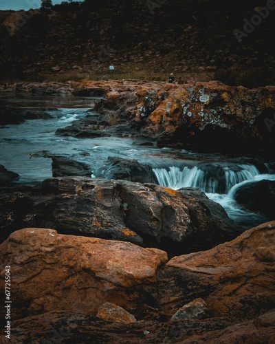Vertical of a cascade flowing through rocks on a cloudy day shot in long exposure