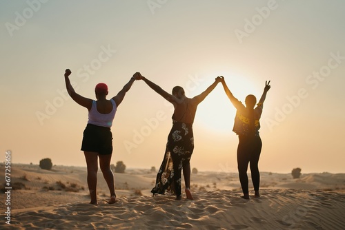 Back view of three female friends with the hands up and together in the desert under bright sun