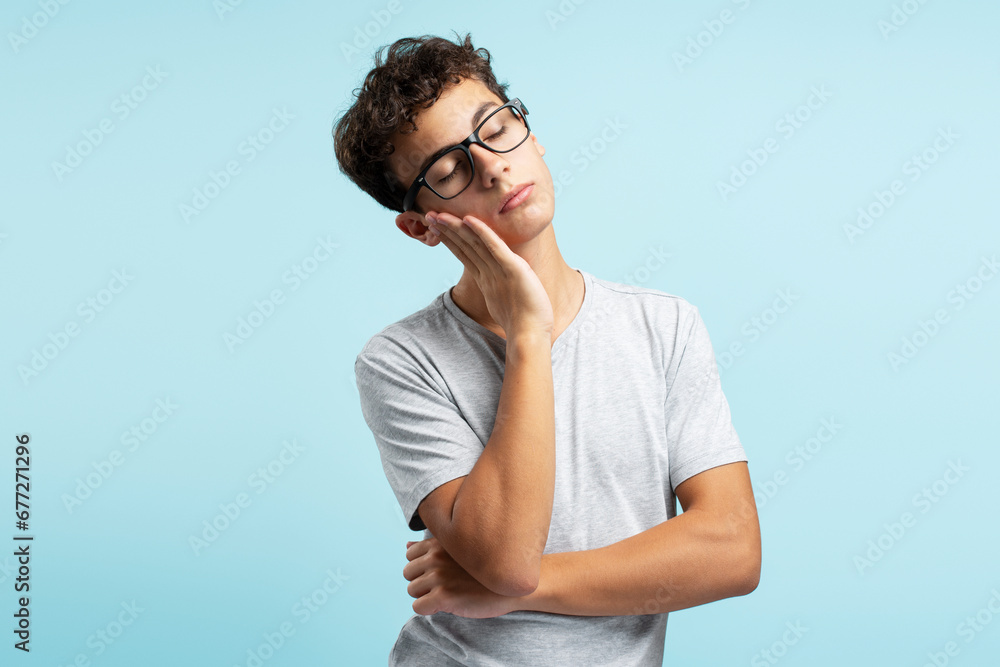Portrait of sad tired teenage boy wearing glasses with closed eyes isolated on blue background Portrait of sad tired teenage boy wearing glasses with closed eyes isolated on blue background