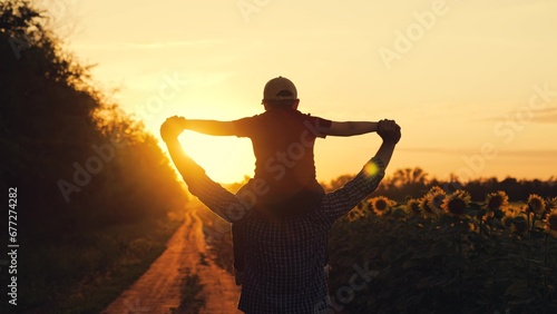 Happy child sitting on fathers shoulders is playing pilot at sun. Family, dad kid son are walking fields with sunflowers play pilots. Family outdoor entertainment. Dream of flying concept. Superhero