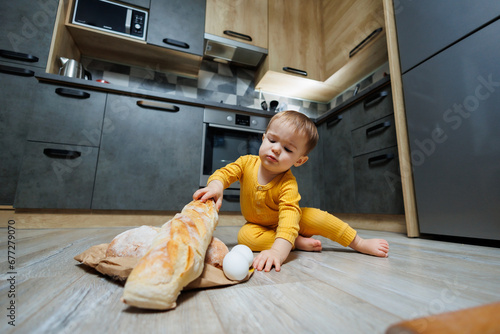 A little boy 1 year old is sitting in the kitchen with fresh bread. Child with bread on the floor.