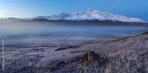 Blue hour in the mountains. Autumn frost on dry grass. Snowy pea