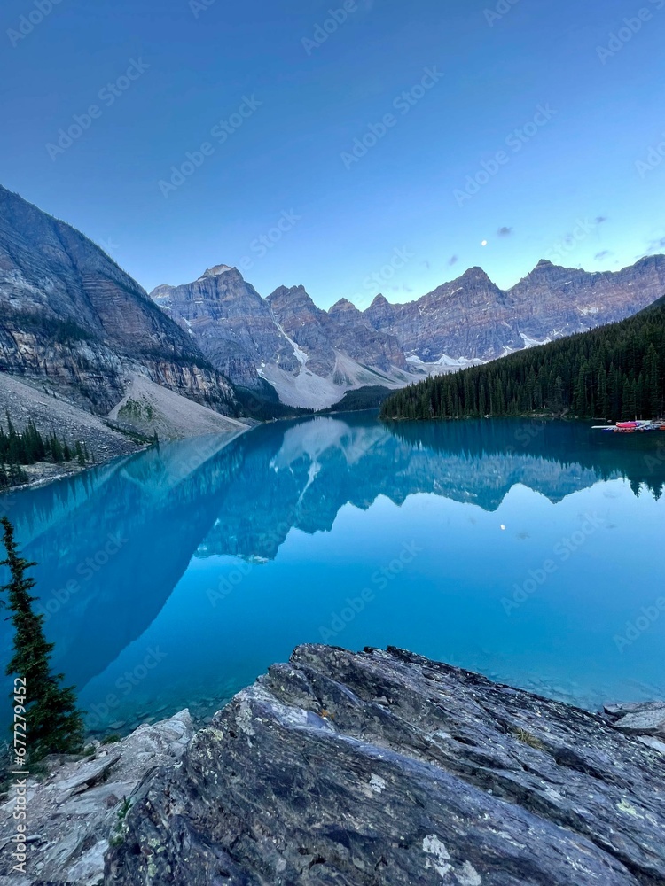 Vertical shot of a clear blue lake surrounded by a forest and a mountain range in the background
