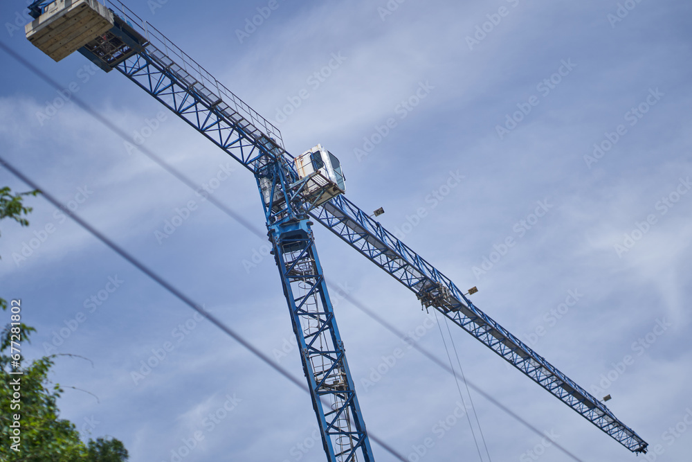 One modern tall crane against a clear blue sky. Construction crane and the upper part of the building with scaffolding. High quality photo