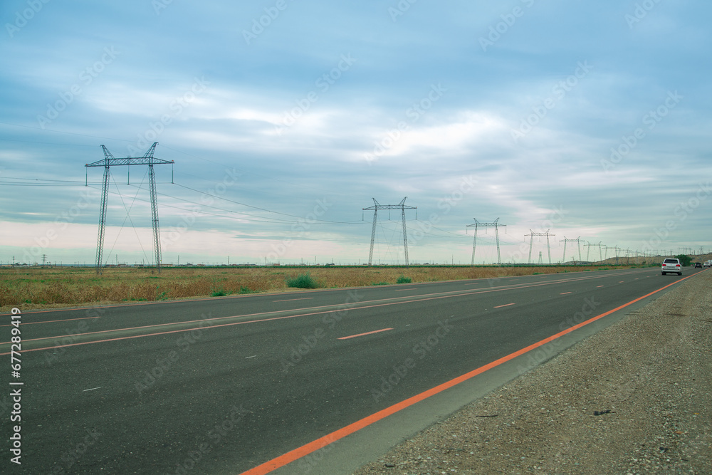 Electric transmission lines along the road in the steppe against the backdrop of the sunset blue sky.